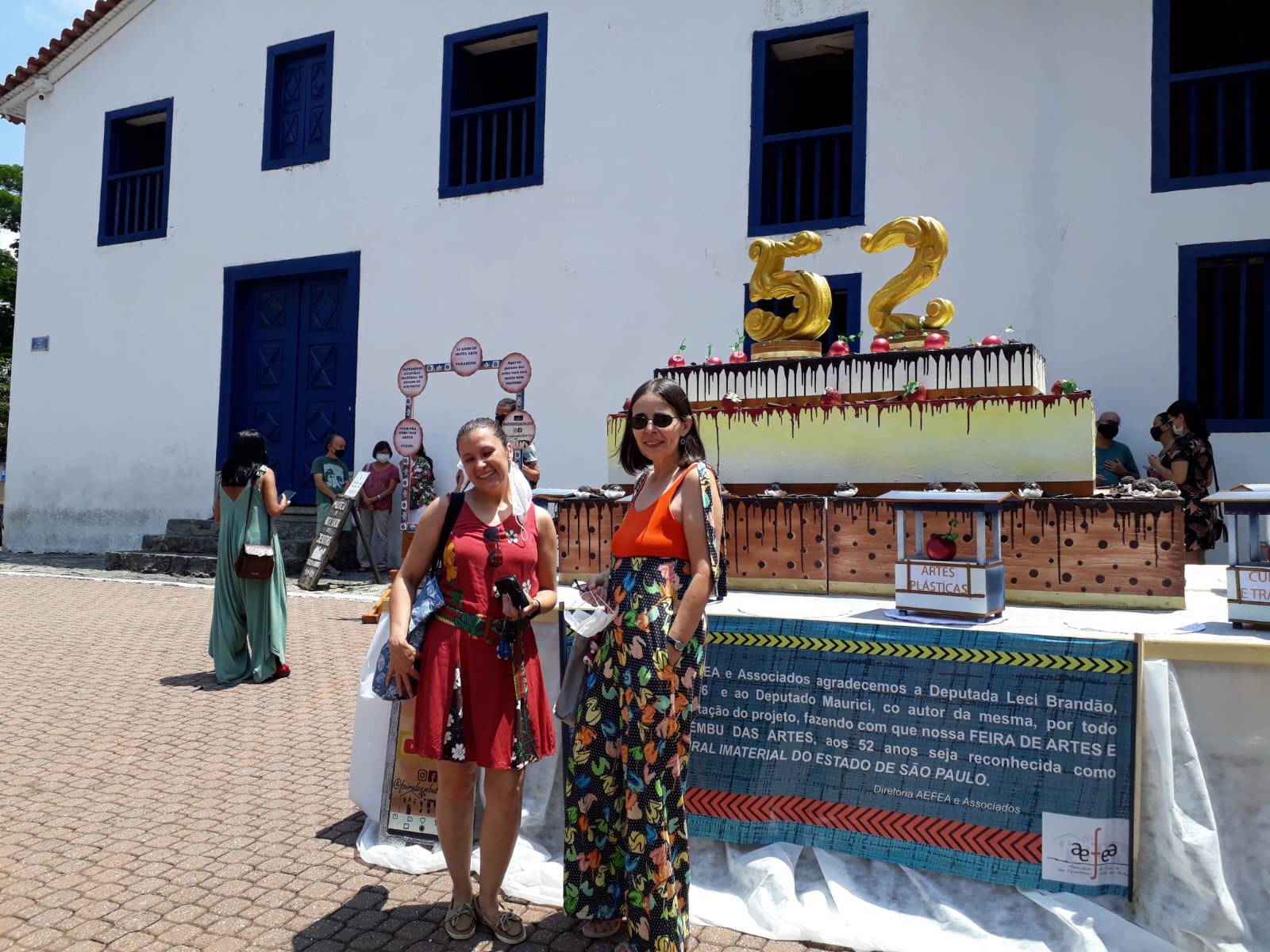 Um bolo cenográfico em frente ao Museu de Arte Sacra, e turistas fotografando o momento qe celebrava 52 anos da Feira e o reconhecimento como Patrimônio Cultural em 2021.
